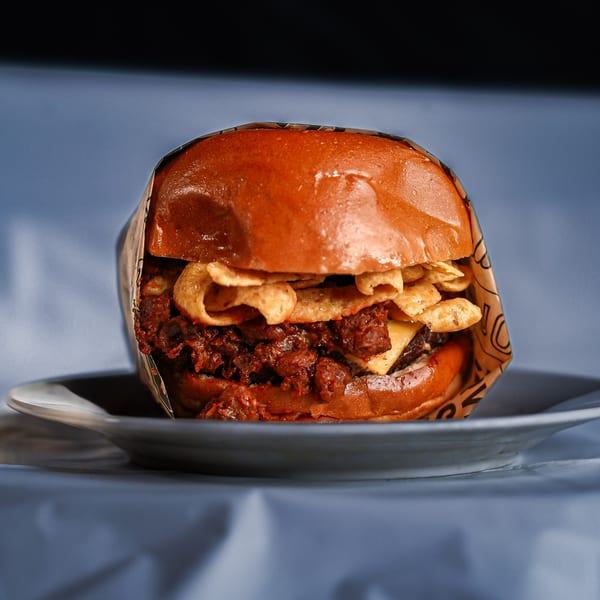 Close-up of a burger with pulled pork, cheese, and crispy chips, wrapped in paper on a plate.
