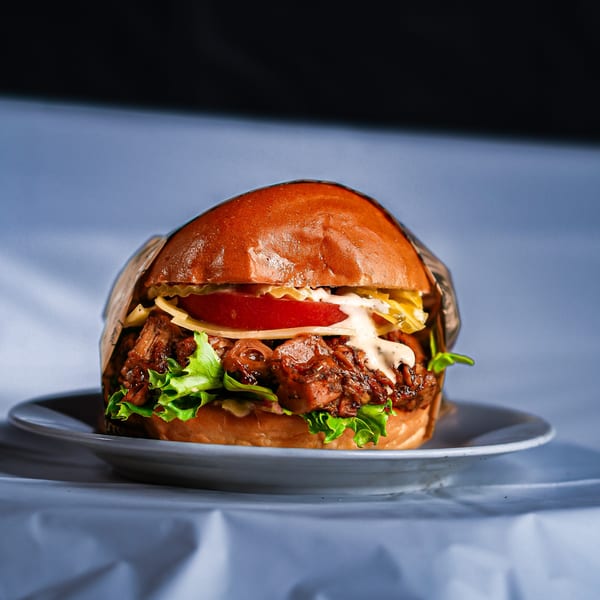 Close-up of a gourmet burger with pulled meat, lettuce, tomato, cheese, and sauce on a bun.
