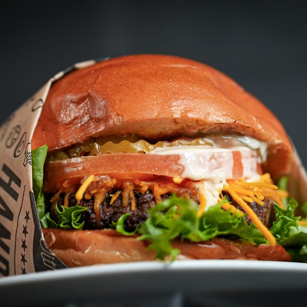 Close-up of a gourmet burger with lettuce, tomato, pickles, cheese, and sauce on a bun.