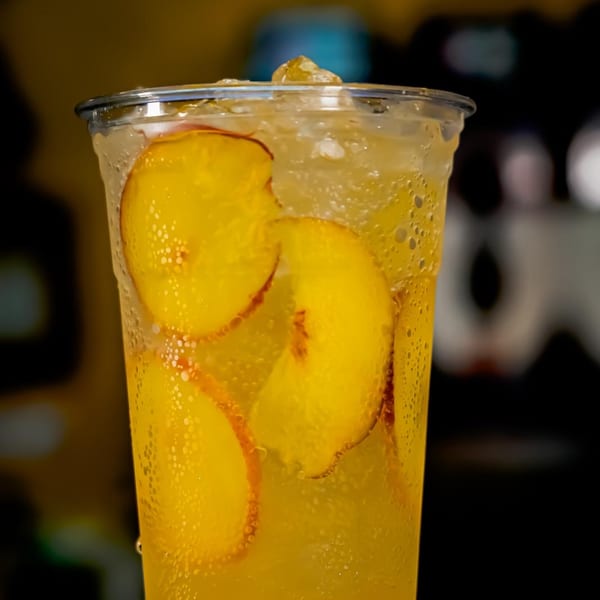 Close-up of a cold peach drink with ice and peach slices in a clear plastic cup.